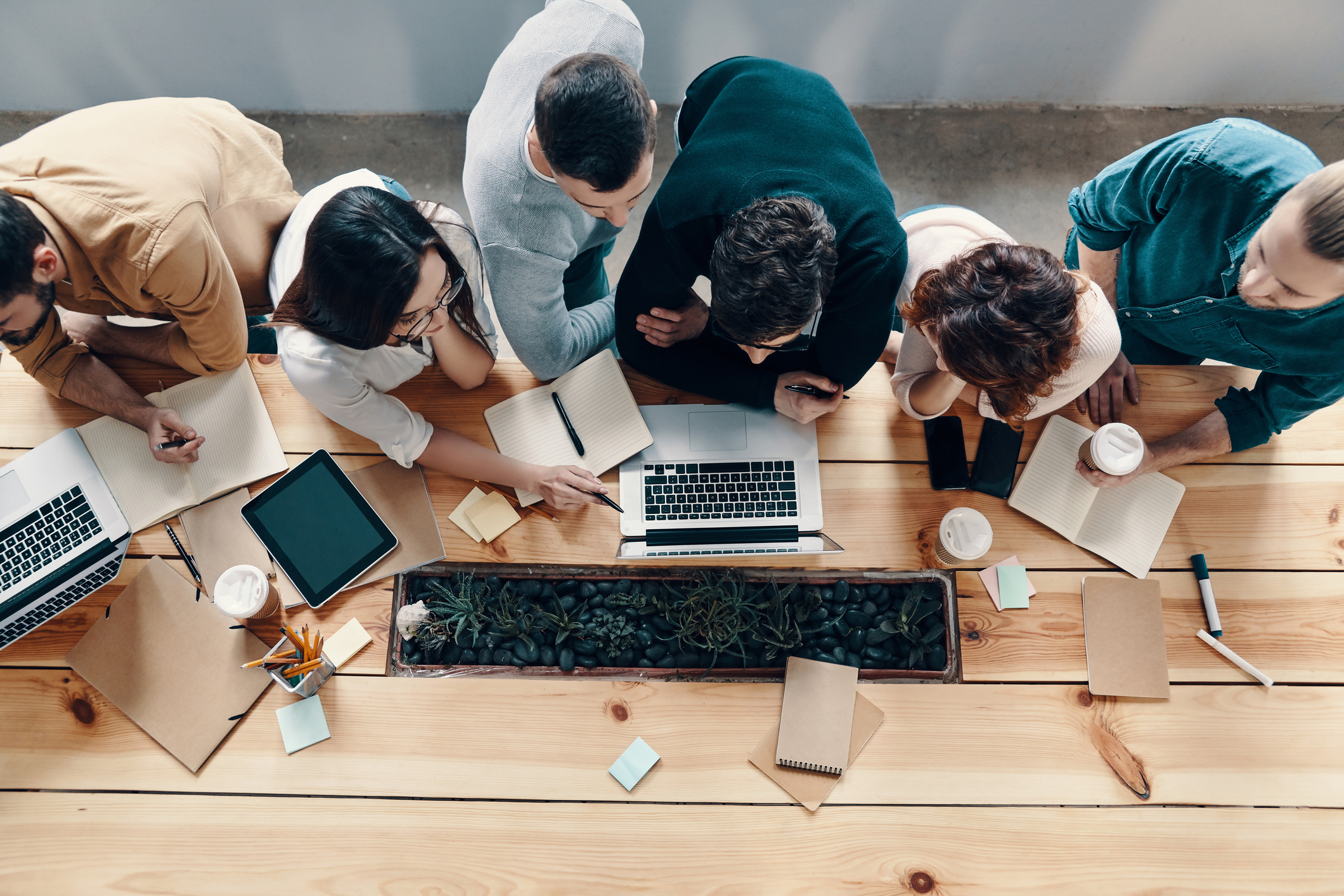 Top view of young modern people in smart casual wear using modern technologies while working in the creative office